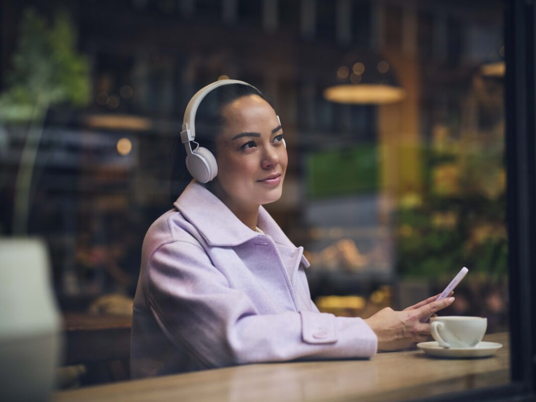 Kvinne som koser seg med å høre lydbok på en hyggelig kafe
