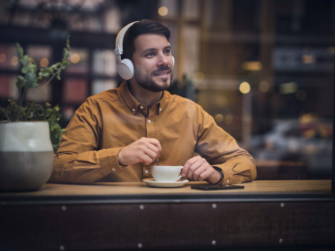 Mann som lytter til lydbok mens han sitter på kafé